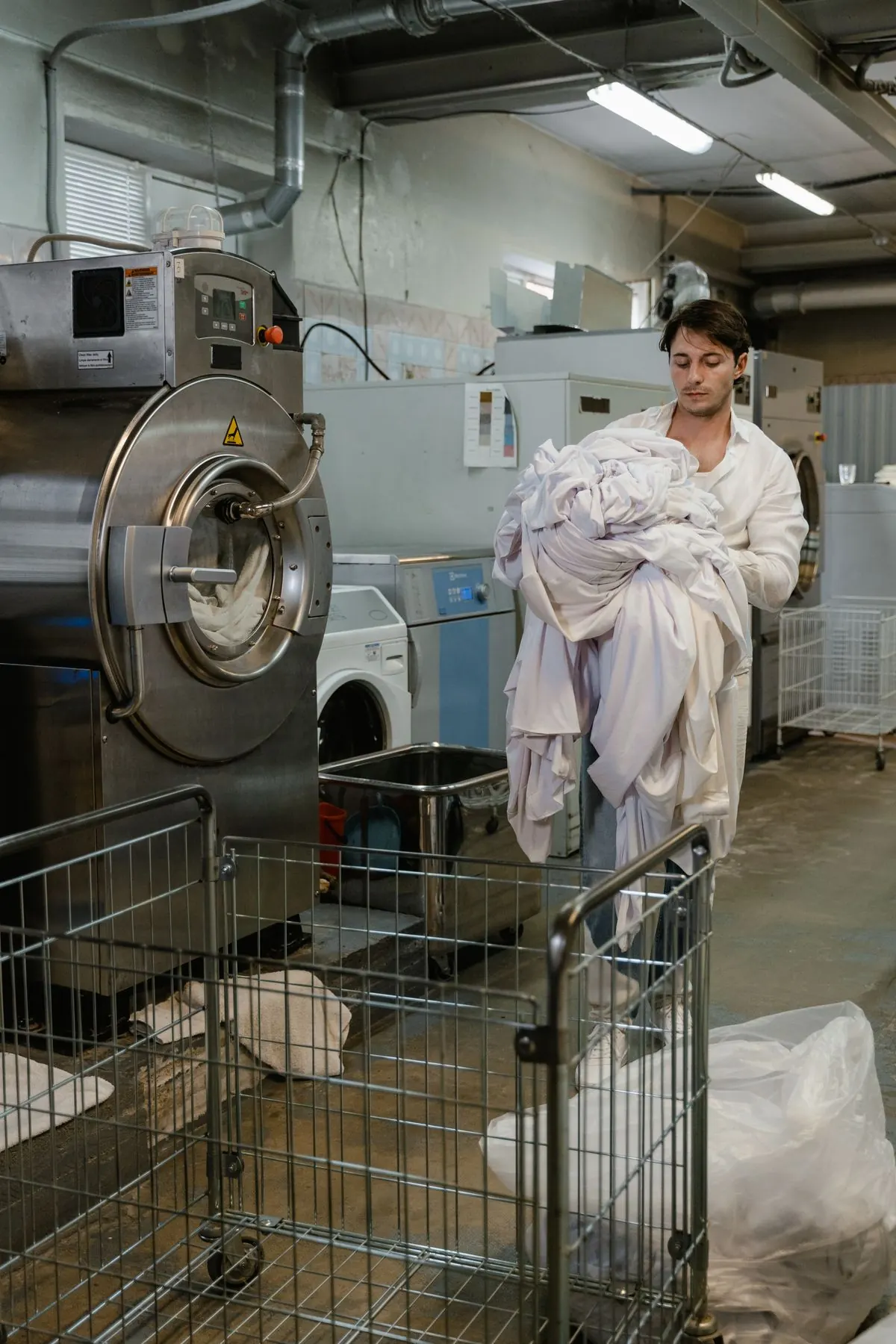 Employé portant du linge dans une blanchisserie équipée de machines professionnelles